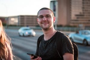 Cyberpunk Garrett Mickley, a white man with short hair standing on a bridge with cars in the background.