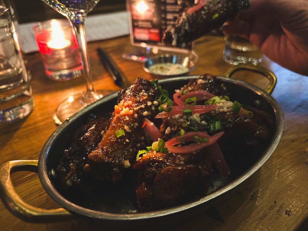 Photograph of a crock of chicken wings wit a raspberry sauce.